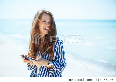 smiling stylish female on seacoast with smartphone smiling stylish female on seacoast with smartphone 114266776