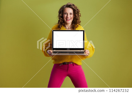 smiling fit female showing laptop blank screen against green 114267232