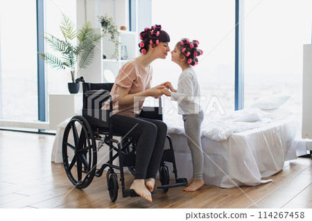 Young mother in wheelchair holds hands of her little daughter on weekend. Young mother in wheelchair holds hands of her little daughter on weekend. 114267458