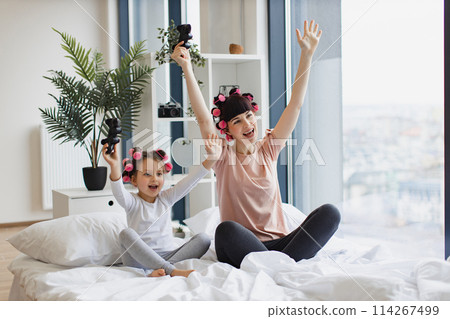 Happy mother and daughter raise their hands up after winning a video game. 114267499