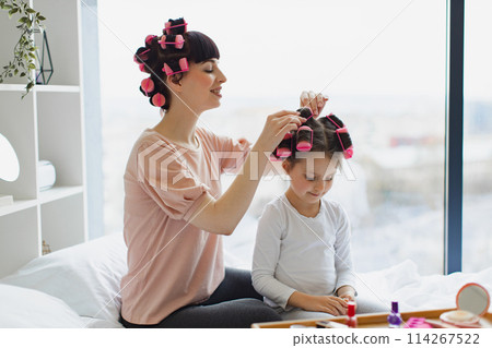 Mom and daughter make a fashionable hairstyle using curlers. Mom and daughter make a fashionable hairstyle using curlers. 114267522