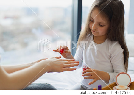 Cute little girl learns to paint her nails by applying polish on mother hands. 114267534