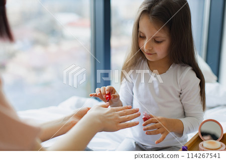Cute little girl learns to paint her nails by applying polish on mother hands. 114267541