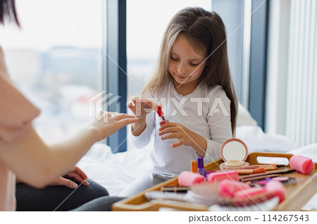 Cute little girl learns to paint her nails by applying polish on mother hands. Cute little girl learns to paint her nails by applying polish on mother hands. 114267543