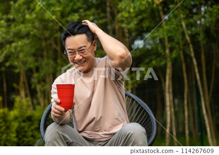 Man sitting on nature with beverage expressing cheerful expression during picnic 114267609