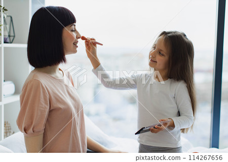 Close up portrait of Caucasian daughter applying powder on her young mom's face. 114267656