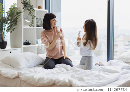 Young mother sings with her little adorable daughter using combs. 114267784