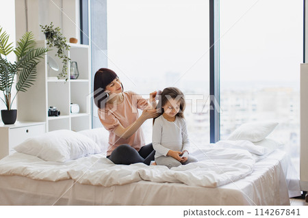Yong mother in casual outfit brushing her little daughter's hair. Yong mother in casual outfit brushing her little daughter's hair. 114267841