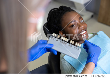 Dentist choosing the color for tooth implant for the female patient 114267880