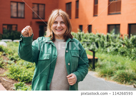 Attractive young woman in glasses showing key while standing outdoor against new house. Real estate agent holding key on street background Attractive young woman in glasses showing key while standing outdoor against new house. Real estate agent holding key on street background 114268593