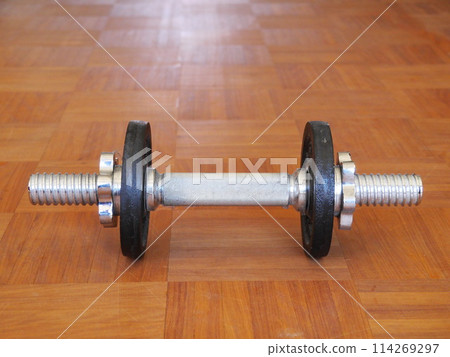 A silver dumbbell is sitting on a wooden floor A silver dumbbell is sitting on a wooden floor 114269297