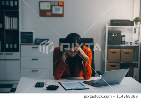 Portrait of tired young business Asian woman work with documents tax laptop computer in office. Sad, unhappy, Worried, Depression, or employee life stress concept 114269369