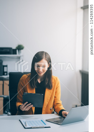 Attractive smiling young asian business woman wear glasses work at home office, Asian woman working on laptop computer holding tablet.business finance concept. 114269395