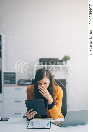 Portrait of tired young business Asian woman work with documents tax laptop computer in office. Sad, unhappy, Worried, Depression, or employee life stress concept 114269407