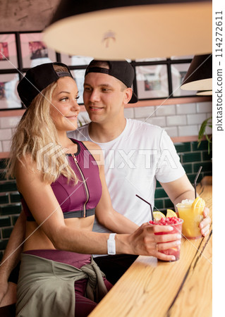 Sportive couple sitting in a cafe enjoying fresh drinks after intensive workout. Sportive couple sitting in a cafe enjoying fresh drinks after intensive workout. 114272611