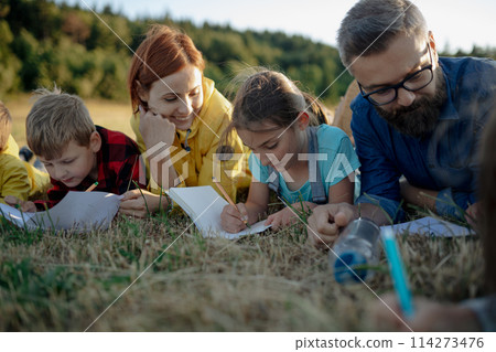 Young students learning about nature, forest ecosystem during biology field teaching class, writing notes. Teachers talking with children during outdoor active education. Young students learning about nature, forest ecosystem during biology field teaching class, writing notes. Teachers talking with children during outdoor active education. 114273476