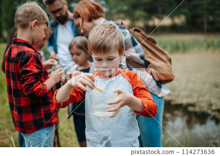 Young students analyzing water quality, ph level with indicator strips during biology field teaching class. Female teacher during outdoor active education. 114273636