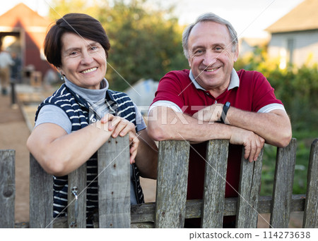 Portrait of a happy elderly couple in the garden near fence of their farm Portrait of a happy elderly couple in the garden near fence of their farm 114273638