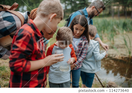 Young students analyzing water quality, ph level with indicator strips during biology field teaching class. Female teacher during outdoor active education. 114273640