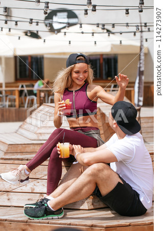 Sportive couple sitting in a cafe enjoying fresh drinks after intensive workout. 114273907