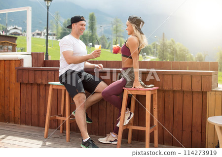 Sportive couple sitting in a cafe enjoying fresh drinks after intensive workout. Sportive couple sitting in a cafe enjoying fresh drinks after intensive workout. 114273919