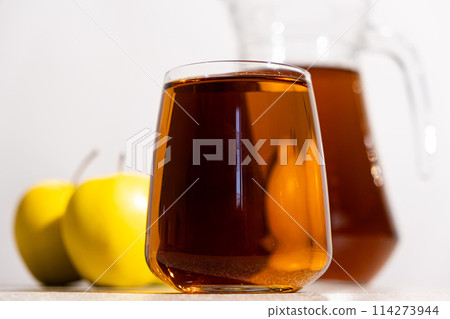 Apple juice in a glass and jug on a white background Apple juice in a glass and jug on a white background 114273944