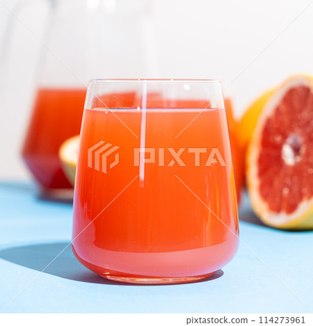 Grapefruit juice in a glass among fresh grapefruits on blue and white background Grapefruit juice in a glass among fresh grapefruits on blue and white background 114273961