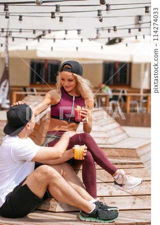 Sportive couple sitting in a cafe enjoying fresh drinks after intensive workout. Sportive couple sitting in a cafe enjoying fresh drinks after intensive workout. 114274033