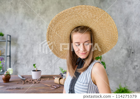 Portrait of Woman gardener transplanting plants. Concept of home garden. Flower and garden shop. A straw hat with a wide brim. 114275379