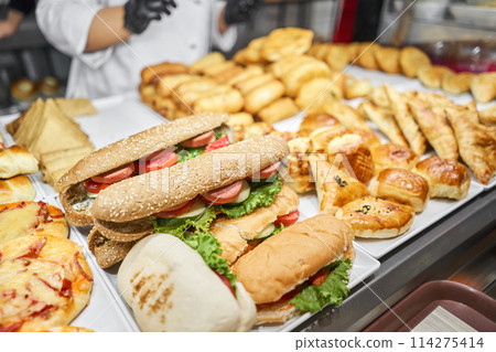 Fresh sandwiches, pies and pizza to choose from in the window of a cafe, buffet or self-service cafe. Croissant with ham and cheese. Hot pastries lie on the shelf in the cafe. Buns in the store. Fresh sandwiches, pies and pizza to choose from in the window of a cafe, buffet or self-service cafe. Croissant with ham and cheese. Hot pastries lie on the shelf in the cafe. Buns in the store. 114275414