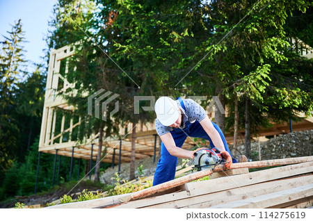 Carpenter using circular saw for cutting wooden plank. Man worker building wooden frame house. The ideology behind modern, environmentally-conscious construction. Carpenter using circular saw for cutting wooden plank. Man worker building wooden frame house. The ideology behind modern, environmentally-conscious construction. 114275619