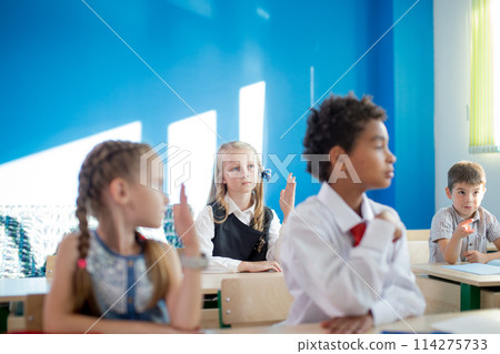 group of school children all raising their hands in the air to answer 114275733