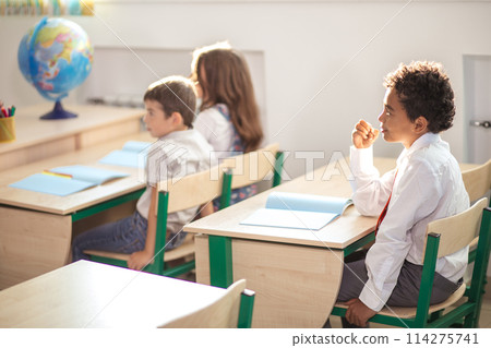 school boy sitting in desk and thinking while writing exam school boy sitting in desk and thinking while writing exam 114275741