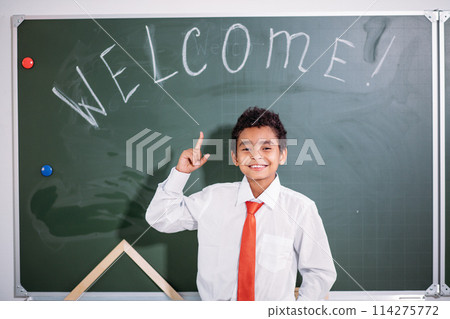 african school boy standing against chalk board with welcome word and looking at camera african school boy standing against chalk board with welcome word and looking at camera 114275772