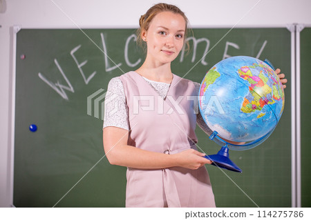 young teacher looking away at desk with globe young teacher looking away at desk with globe 114275786
