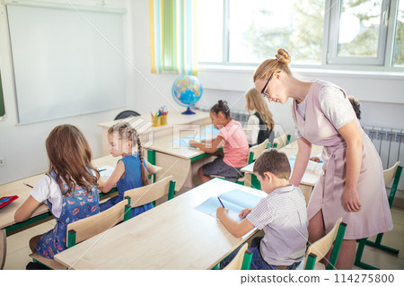 Teacher helping kids with their homework in classroom at school 114275800