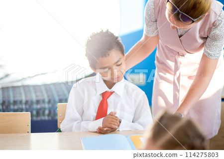 Teacher helping kids with their homework in classroom at school 114275803