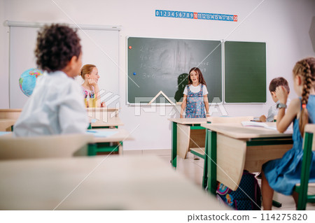 Schoolchild with teacher in classroom. Girl near chalkboard show her homework 114275820