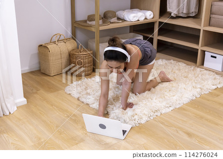 Young Sport Women look at laptop online trainer home fitness workout exercise in living room. Woman using laptop on floor in sportswear arms stretching body weight traning. Healthy lifestyle concept 114276024