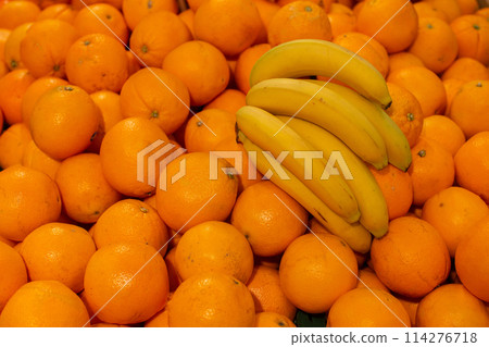 Branch of yellow ripe bananas and orange.Tropical fruits on sale. 114276718