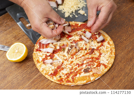 Man's hands add pieces of bacon to pizza. Man's hands add pieces of bacon to pizza. 114277130