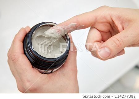 female hand takes a clay face mask from a jar. home spa. close-up female hand takes a clay face mask from a jar. home spa. close-up 114277392