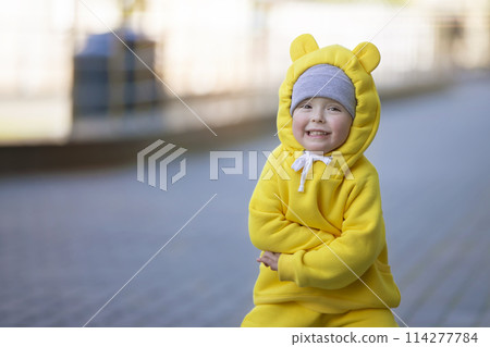 Funny little girl in a warm yellow suit with ears on a walk. 114277784