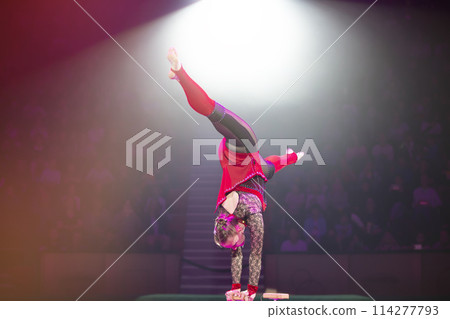 A gymnast performs in a show. A girl gymnast performs a circus acrobatic performance. 114277793