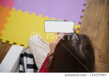 View from above of kid's hands holding smart mobile phone with blank white empty digital touch screen. Mockup. Copy space for mobile application or advertising text. People. Wireless technology View from above of kid's hands holding smart mobile phone with blank white empty digital touch screen. Mockup. Copy space for mobile application or advertising text. People. Wireless technology 114277847