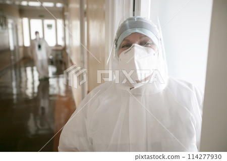 A doctor in a protective medical suit stands on the corridor of the hospital and smiles. 114277930