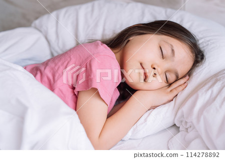Little girl in pink pajamas sleeps in a white bed Little girl in pink pajamas sleeps in a white bed 114278892