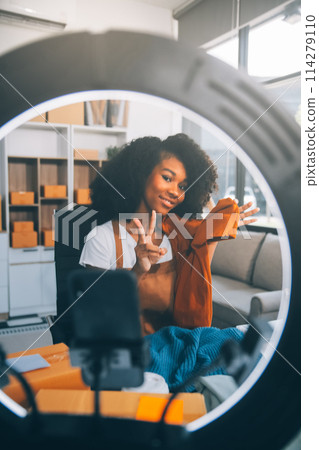 Fashion blogger concept, Young Asian women selling clothes on video streaming.Startup small business SME, using smartphone or tablet taking receive and checking in office 114279110