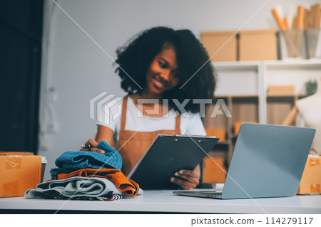 Startup SME small business entrepreneur of freelance Asian woman wearing apron using laptop and box to receive and review orders online to prepare to pack sell to customers, online sme business ideas. 114279117