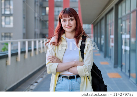 Urban portrait of young confident red-haired female with backpack with crossed arms Urban portrait of young confident red-haired female with backpack with crossed arms 114279782